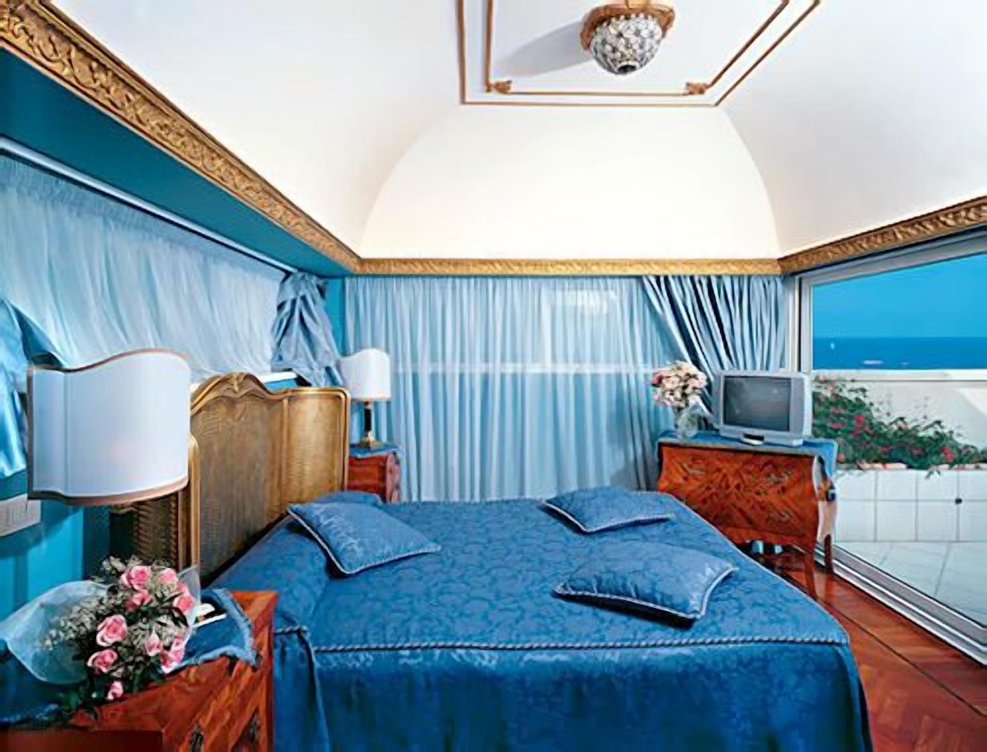 A bedroom with a large bed, a TV, and a view of the sea.