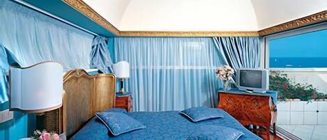 A bedroom with a large bed, a TV, and a view of the sea.