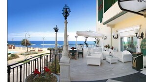 A balcony with white furniture, a view of the sea, and a building with a green awning. - Grand Hotel Michelacci (Gabicce Mare)