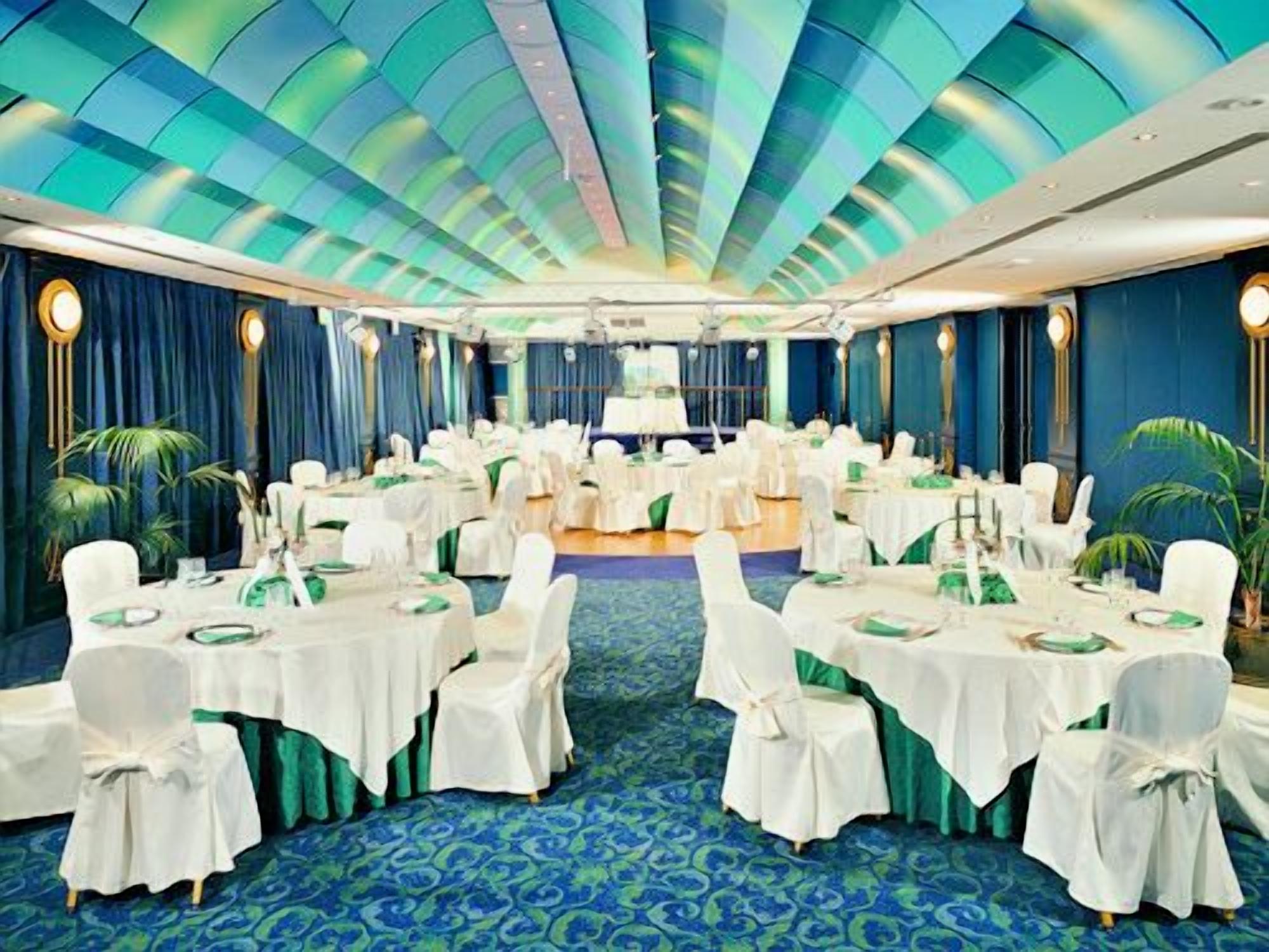 Une salle de banquet avec des tables rondes, des chaises blanches et des rubans verts, aménagée pour un événement officiel.