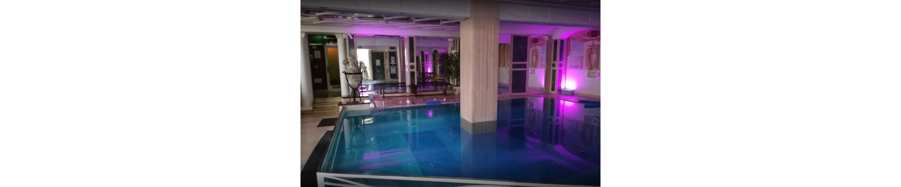 Una piscina interior con barrera de cristal, columnas e iluminación morada.