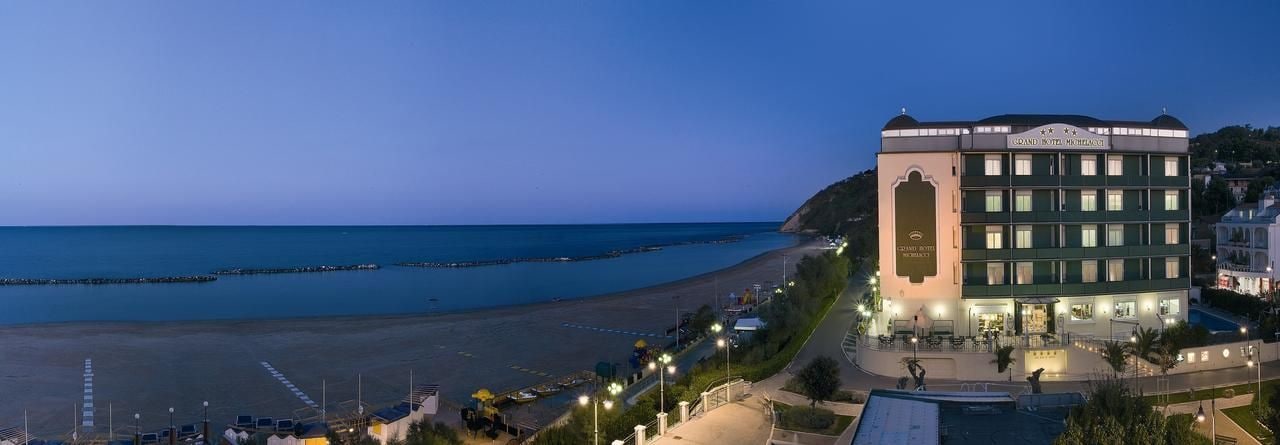 A hotel with a view of the beach and sea, featuring a prominent building with multiple floors and a balcony.
