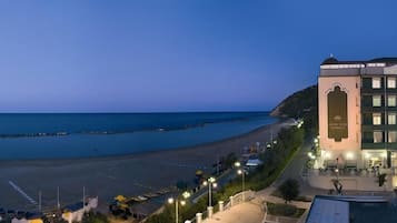 A hotel with a view of the beach and sea, featuring a prominent building with multiple floors and a balcony.
