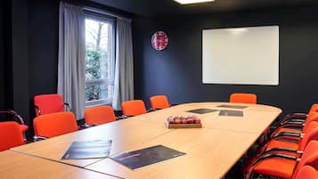 A conference room with a long table, orange chairs, a projector, a clock, and a whiteboard.