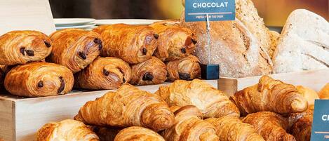 A bakery display with various types of bread and pastries, including croissants and a sign indicating 'Pain au Chocolat'.