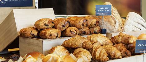 Mostrador de panadería con diversas opciones de panadería, incluyendo cruasanes y pan, con la etiqueta 'FRESHLY BAKED BREAD' y 'PAIN AU CHOCOLAT'.