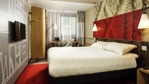 A hotel room with a bed, a desk with a laptop, a TV, and a red carpet. - ibis Swansea (Swansea)