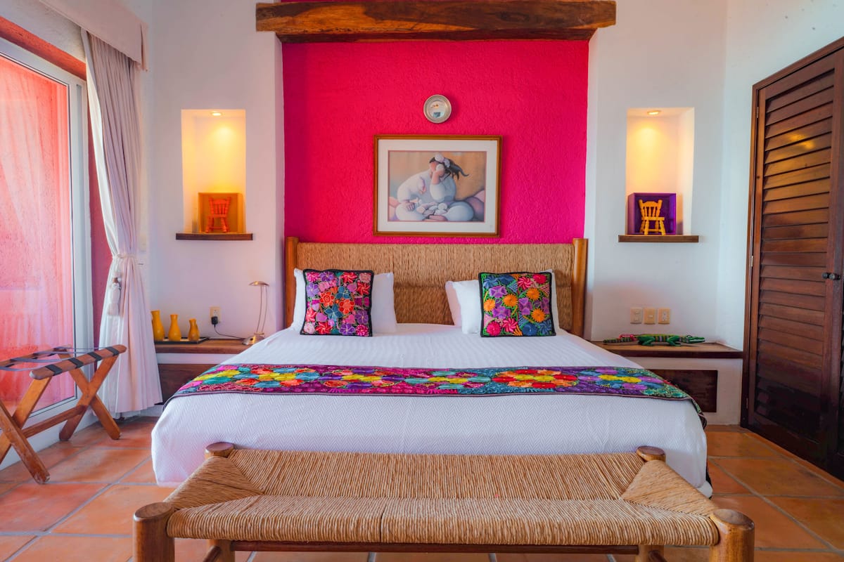 Habitación de hotel con una cama grande, un banco de madera, una pared de acento roja y un cuadro sobre la cama.