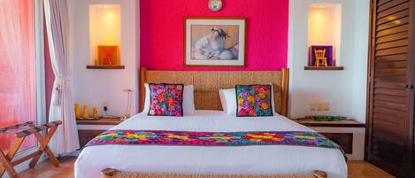 A hotel room with a large bed, a wooden bench, a red accent wall, and a painting above the bed.