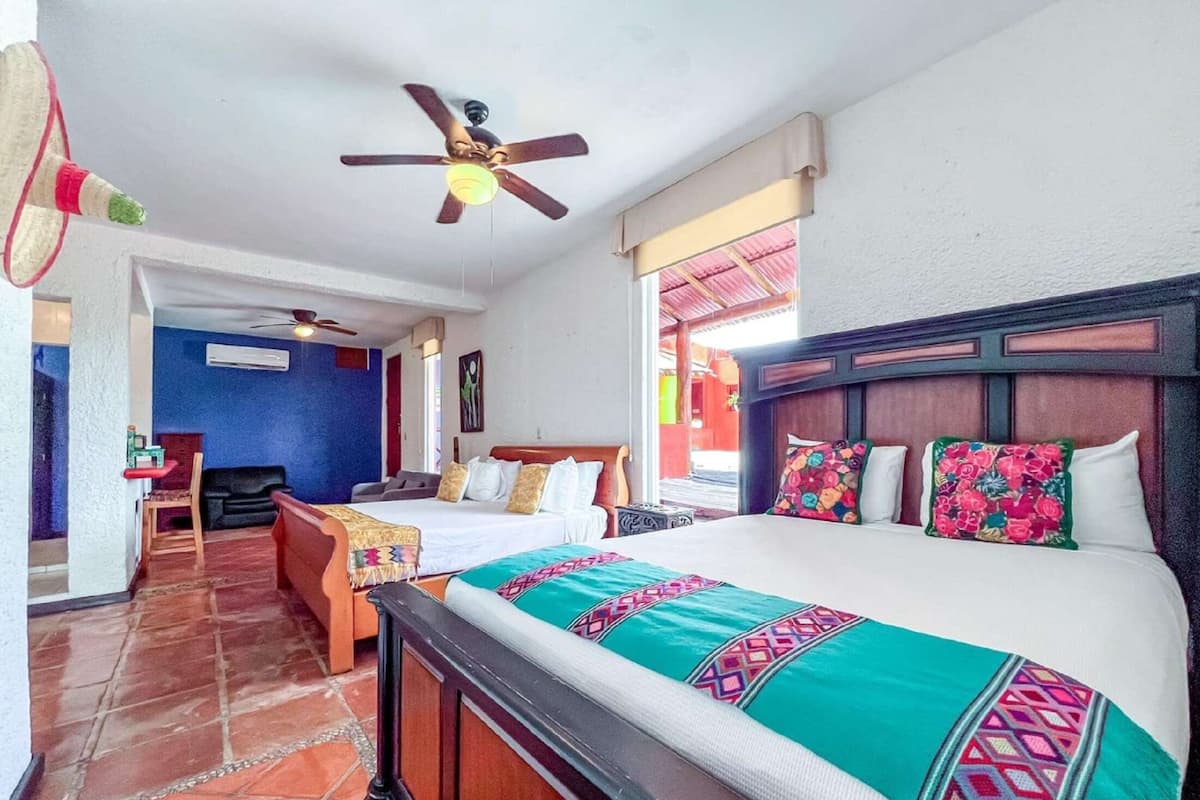 Una habitación de hotel con cama, ventilador de techo, ventana con vistas y suelo de baldosas.