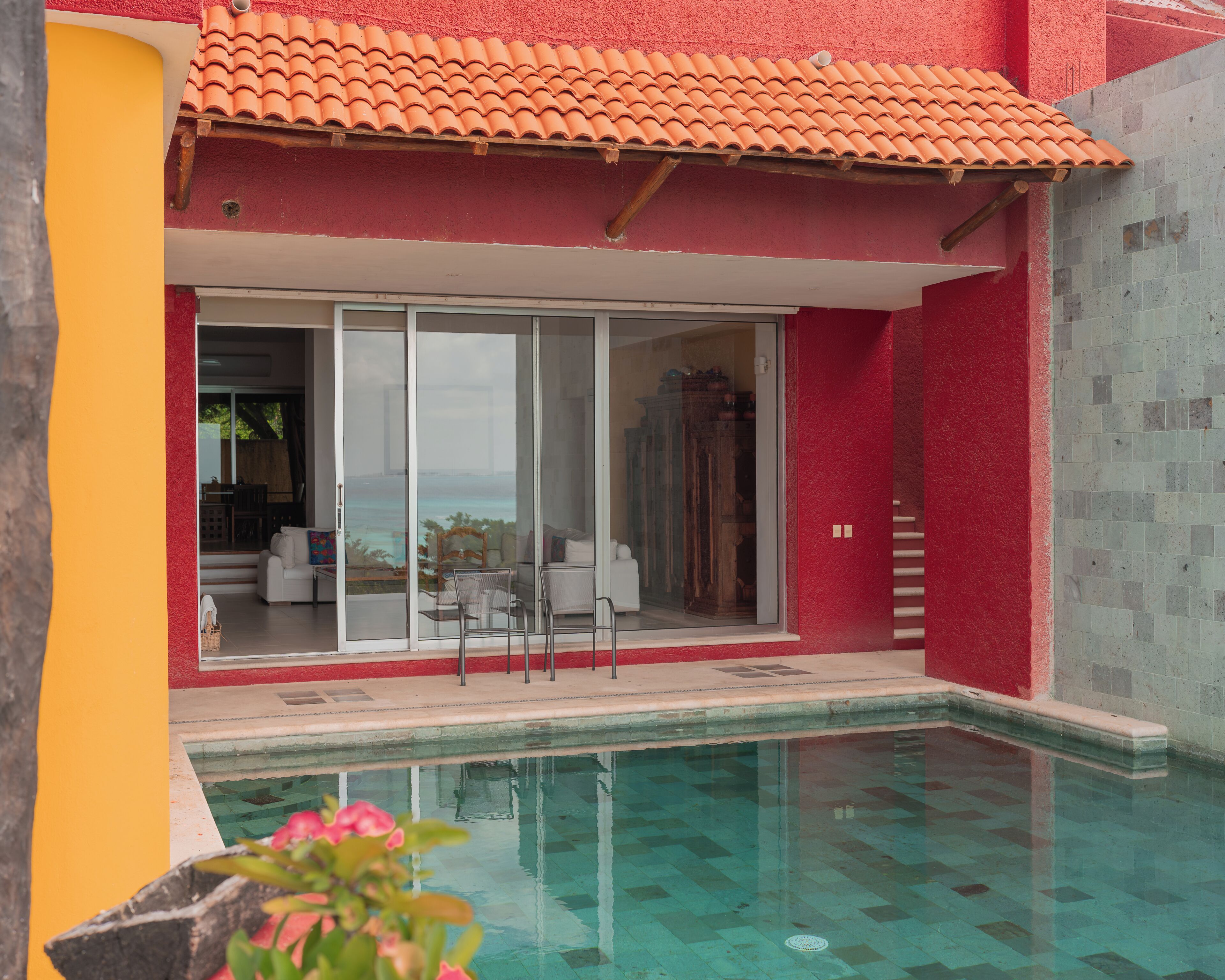 A pool with clear water, a red and yellow building, and a glass door leading to a white interior.