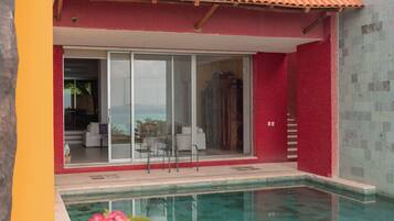 A pool with clear water, a red and yellow building, and a glass door leading to a white interior.