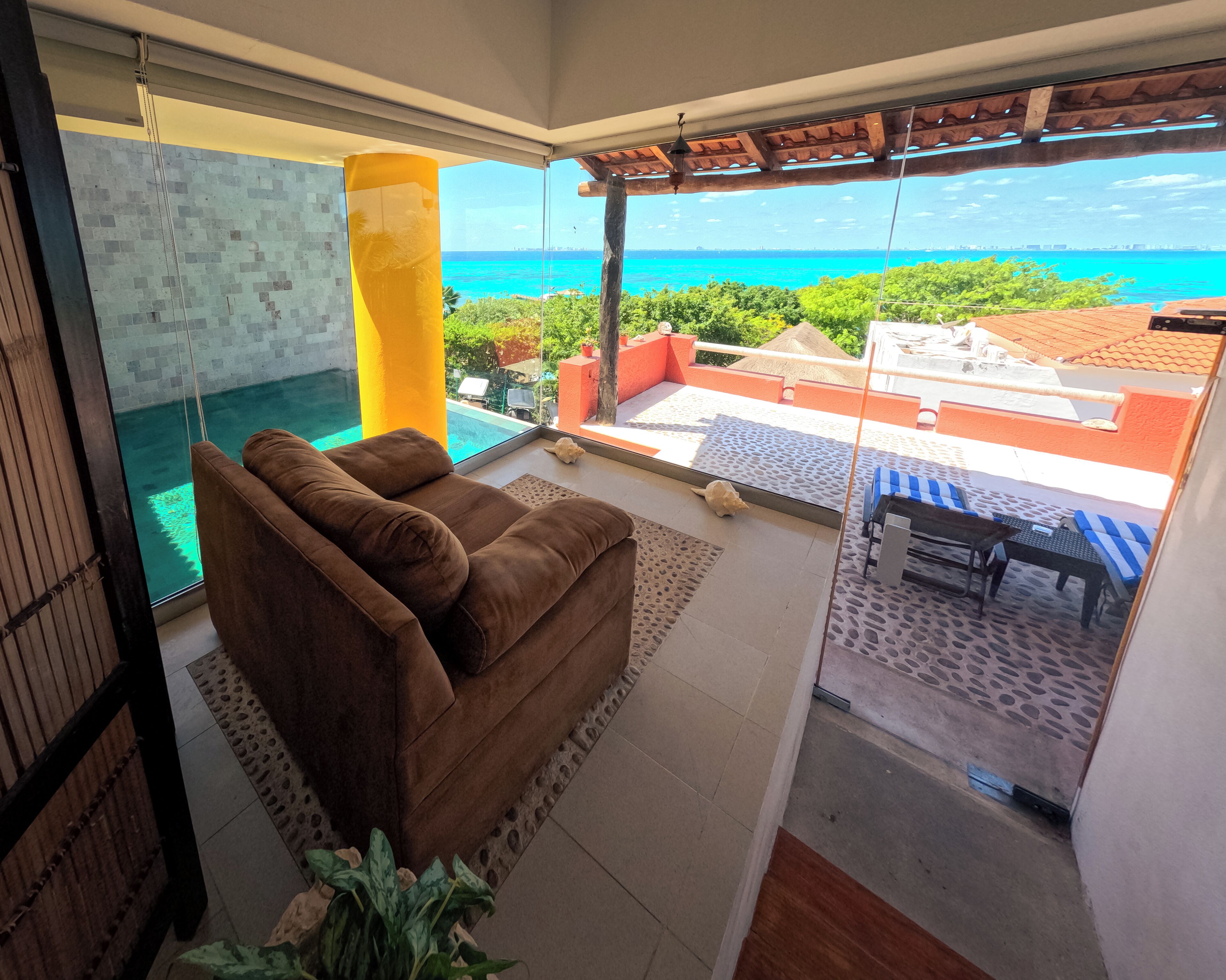 A balcony with a view of the ocean, a brown sofa, and a glass door.