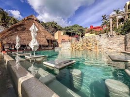 Una piscina con agua cristalina, sombrillas blancas y una estructura de techo de paja.