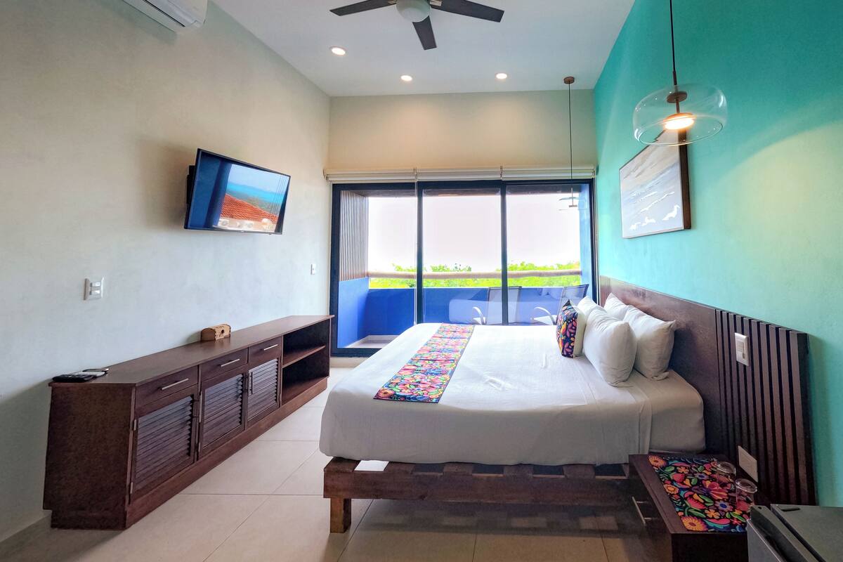 Un dormitorio con cama, televisor, ventilador de techo y ventana con vistas.
