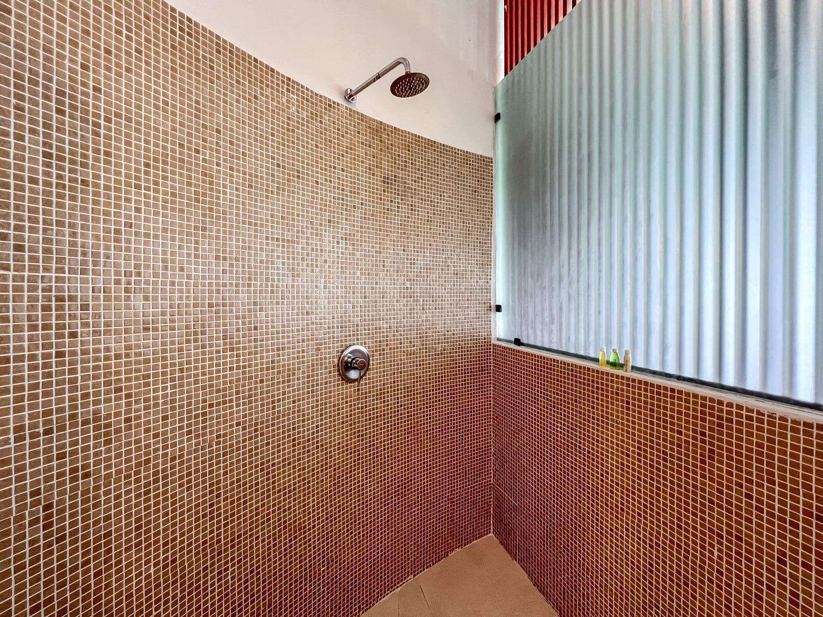 A bathroom with mosaic tile walls, a shower, and a window with blinds.
