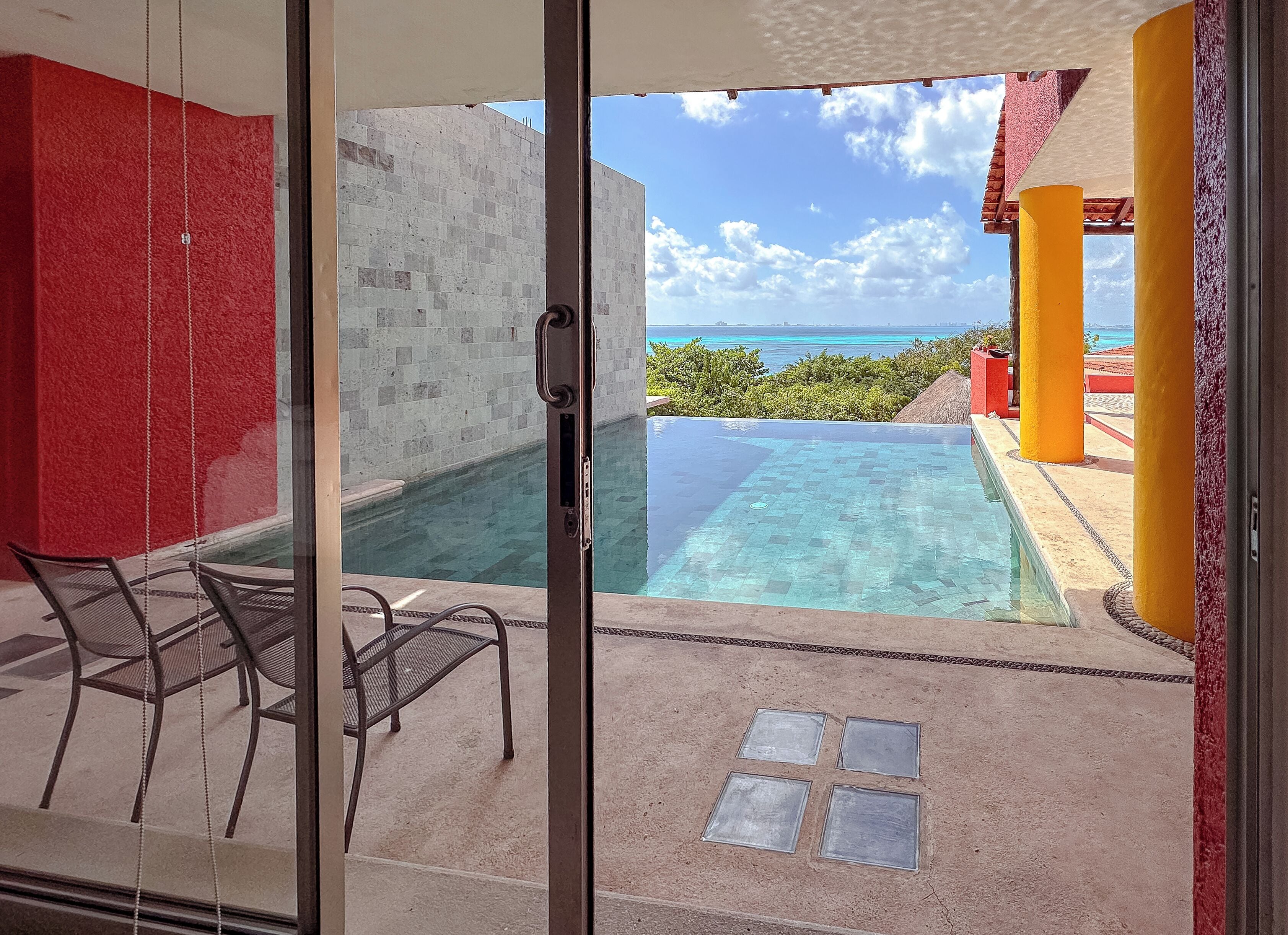 Un balcon fermé par des baies vitrées, avec une piscine, un fauteuil et une vue sur l’océan.