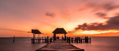 A wooden pier extending into calm waters, leading to a thatched-roof structure.