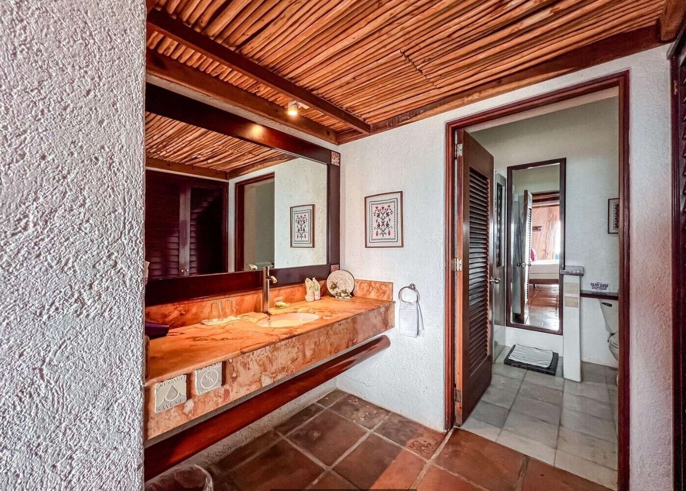 A bathroom with a wooden ceiling, a large mirror, a marble sink, and a tiled floor.