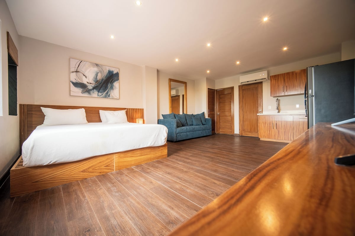 Una habitación de hotel moderna con una cama de madera, un sofá, una zona de cocina y un cuadro abstracto grande en la pared.