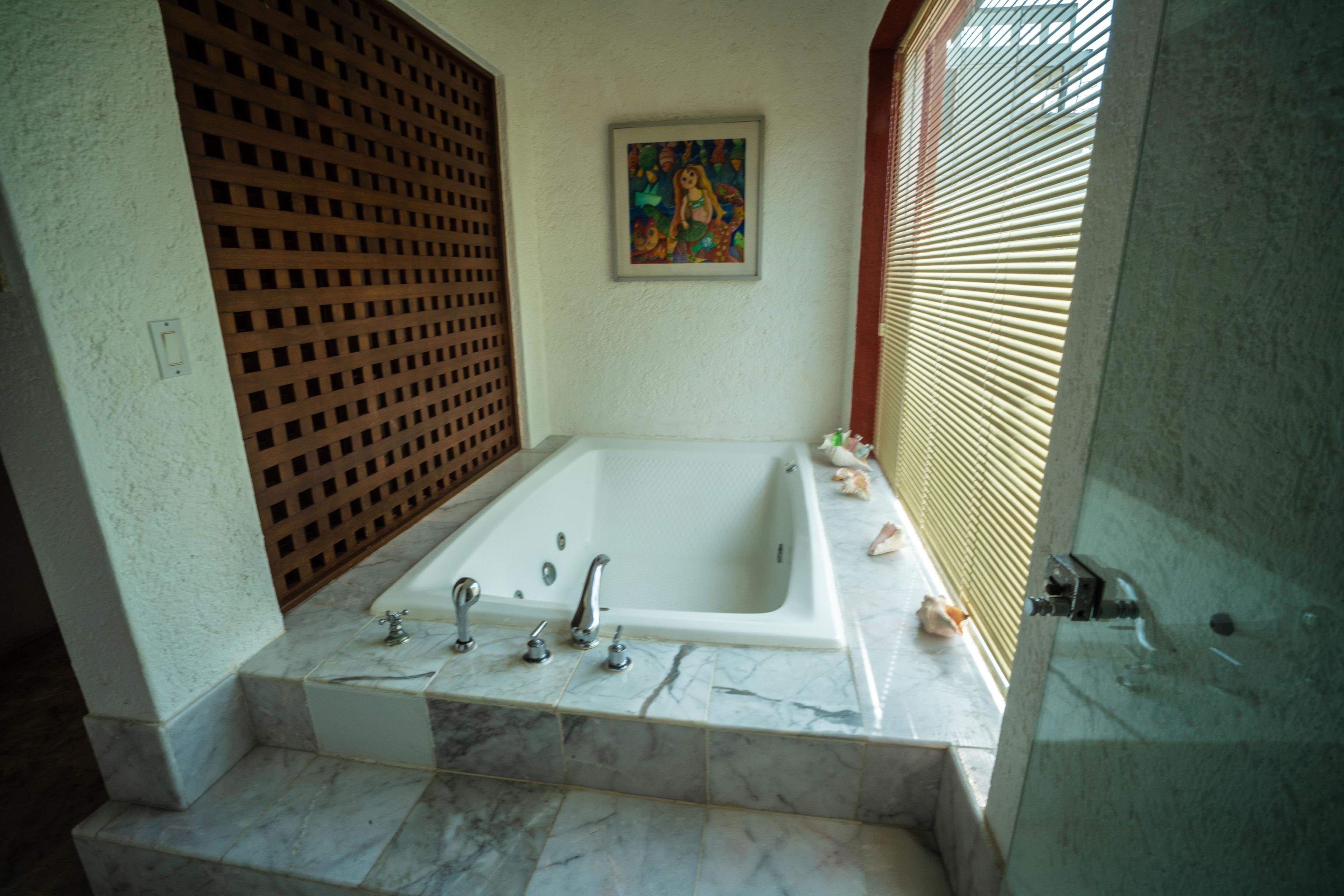 A bathroom with a large bathtub, marble flooring, a wooden lattice partition, and a framed artwork on the wall.