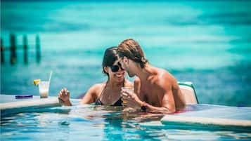 Dos personas en una piscina, con una bebida y un teléfono en el borde.