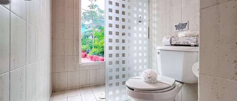 Un baño con inodoro, zona de ducha y ventana con vistas a la vegetación.