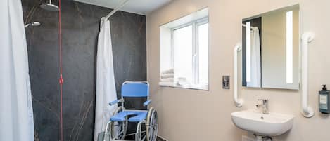Un baño moderno con silla de ruedas, ducha, lavamanos y ventana.