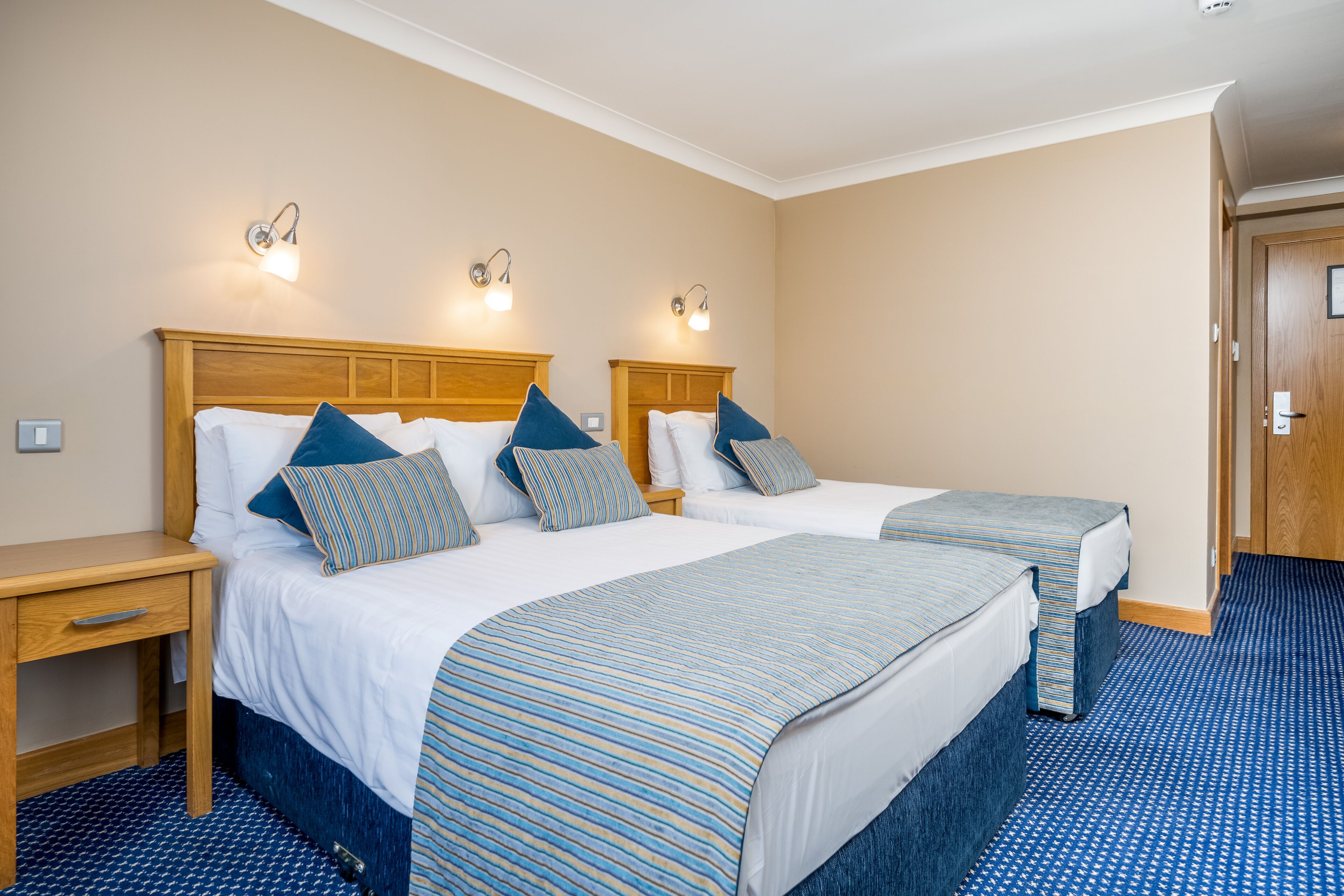 A hotel room with two beds, wooden headboards, and matching blue-striped bedspreads.