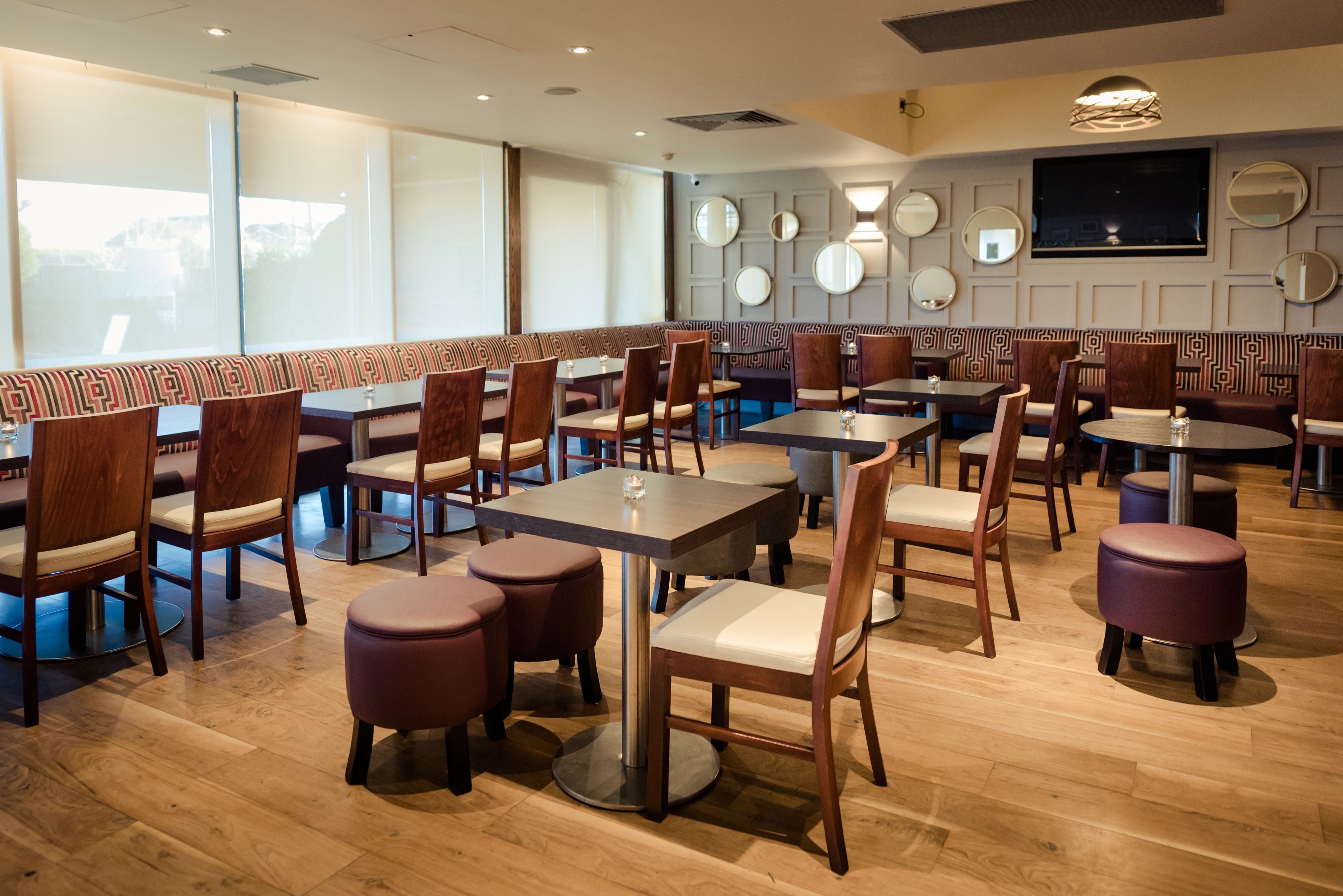 A restaurant with booth seating, round tables, and a wooden floor.