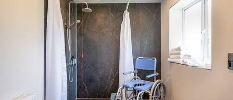 Zona de ducha accesible en silla de ruedas con barra de apoyo, ventana con toallas y radiador.