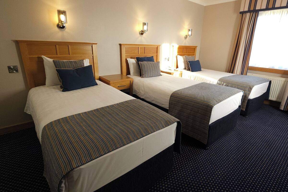 Una habitación de hotel con tres camas individuales, cada una con cabecero y mesitas de noche de madera.