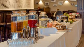 A buffet table with various beverages in glass jars and pitchers, and a selection of bread and pastries.