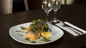 Un plato de comida con un filete de salmón, una rodaja de limón y salsa verde, acompañado de un tenedor y cuchillo sobre una servilleta.