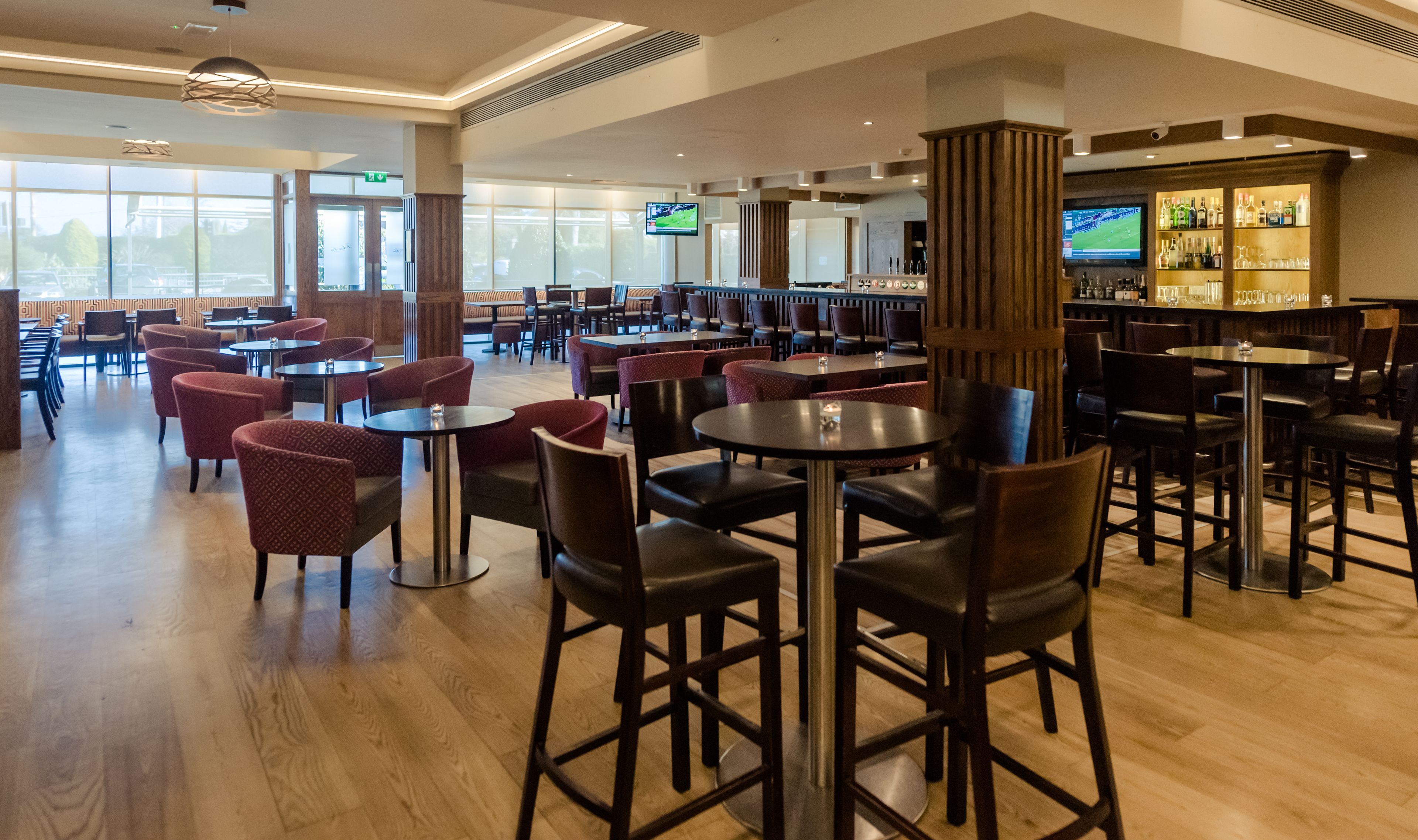 A spacious restaurant with multiple seating areas, including round tables and booths, and a bar area with a variety of bottles and glasses.