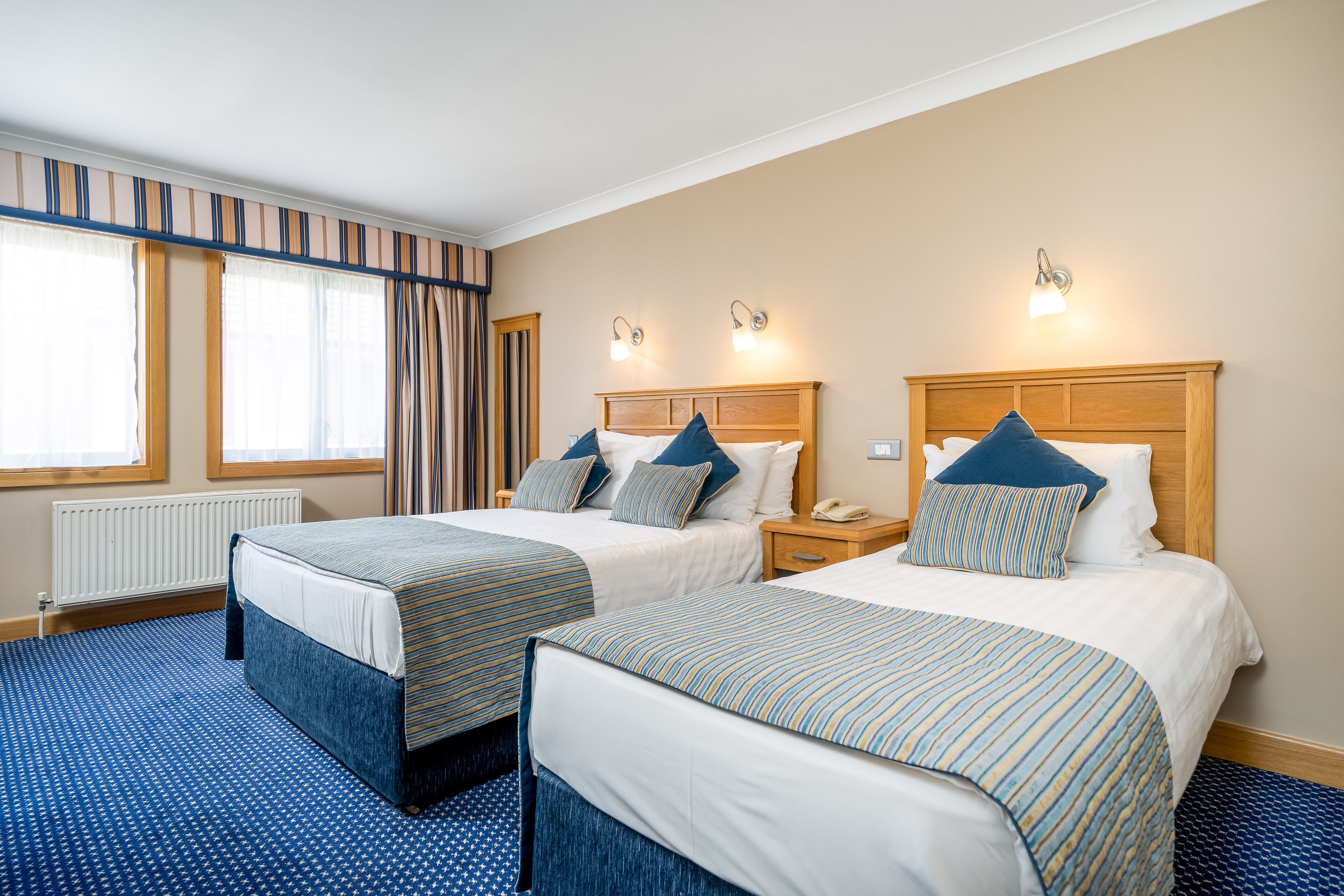 Een hotelkamer met twee bedden, een houten hoofdbord, een nachtkastje en een raam met gordijnen.