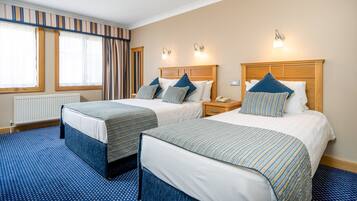 Een hotelkamer met twee bedden, een houten hoofdbord, een nachtkastje en een raam met gordijnen.