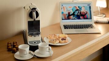 A coffee machine, a laptop, and pastries on a wooden table.