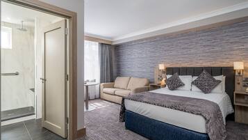 Una habitación de hotel con cama, sofá, una mesita y zona de ducha.