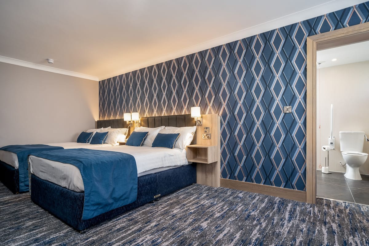 Habitación de hotel con dos camas, un papel tapiz estampado y un cabecero de madera.