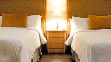 Habitación de hotel con dos camas, una mesita de noche y una lámpara entre ellas.
