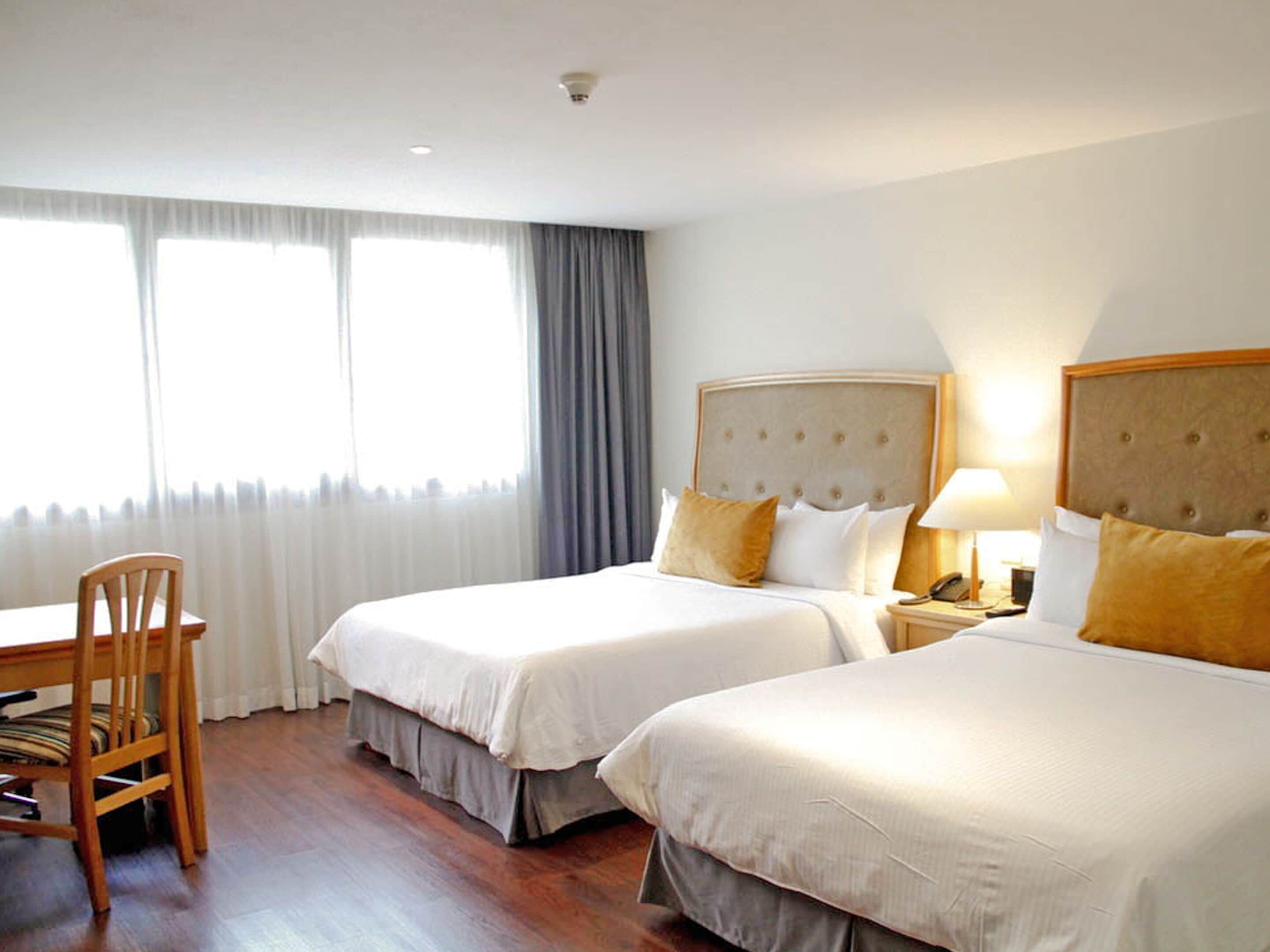 A hotel room with two beds, a desk, a chair, and a window with curtains.