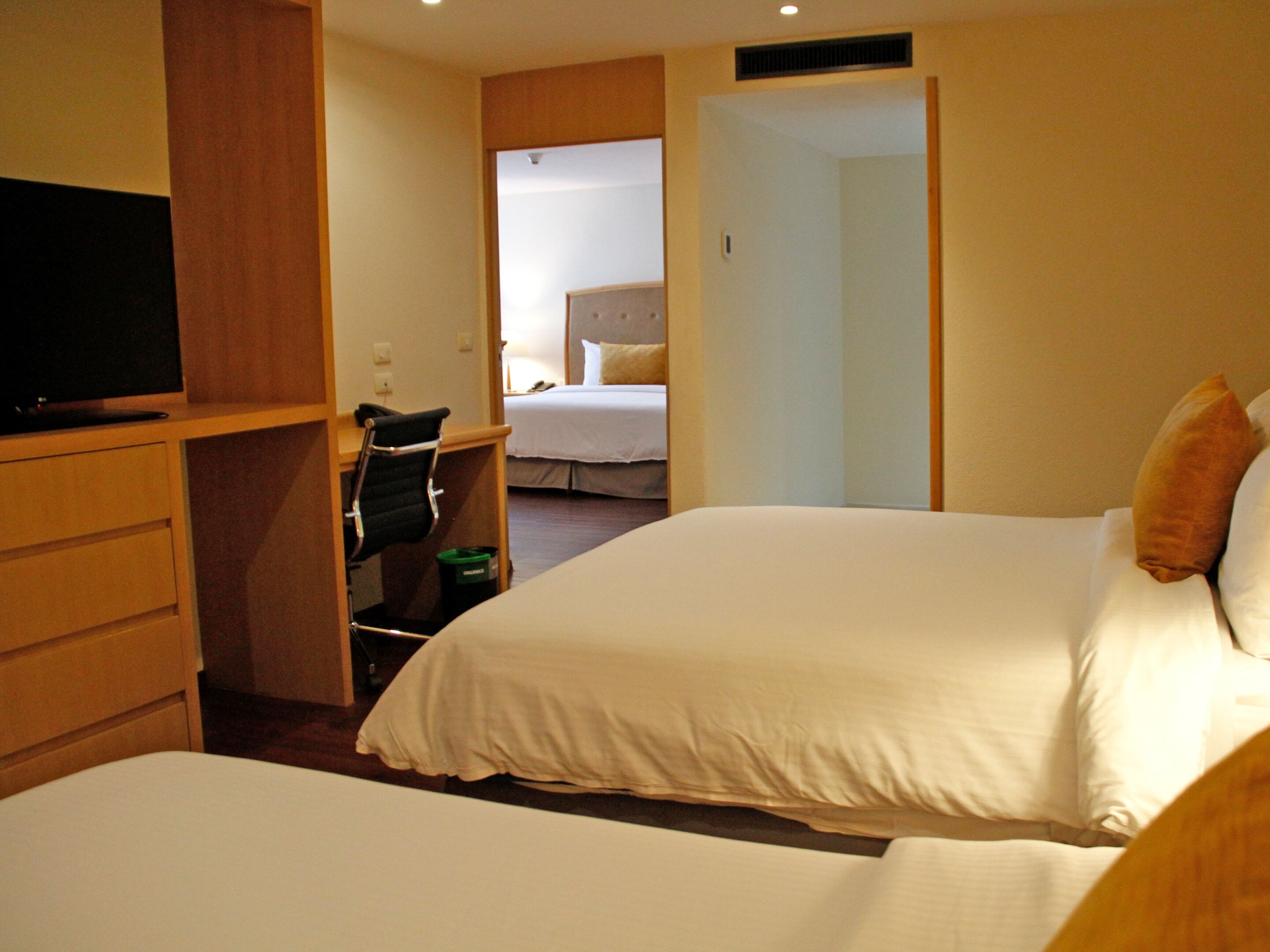 Habitación de hotel con dos camas, un escritorio, una silla, un televisor y un baño visible a través de una puerta abierta.