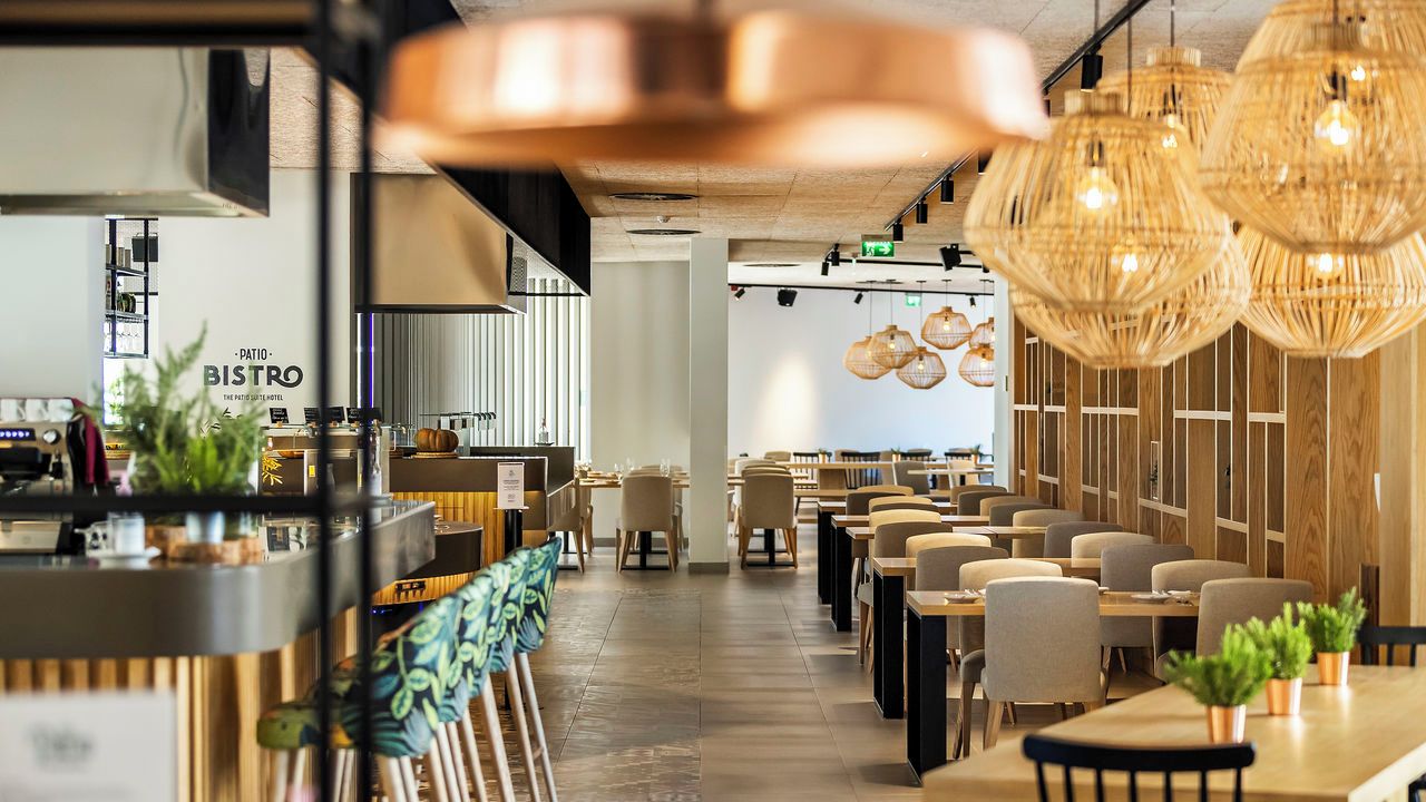A restaurant with a bar area, wooden tables, and hanging light fixtures.