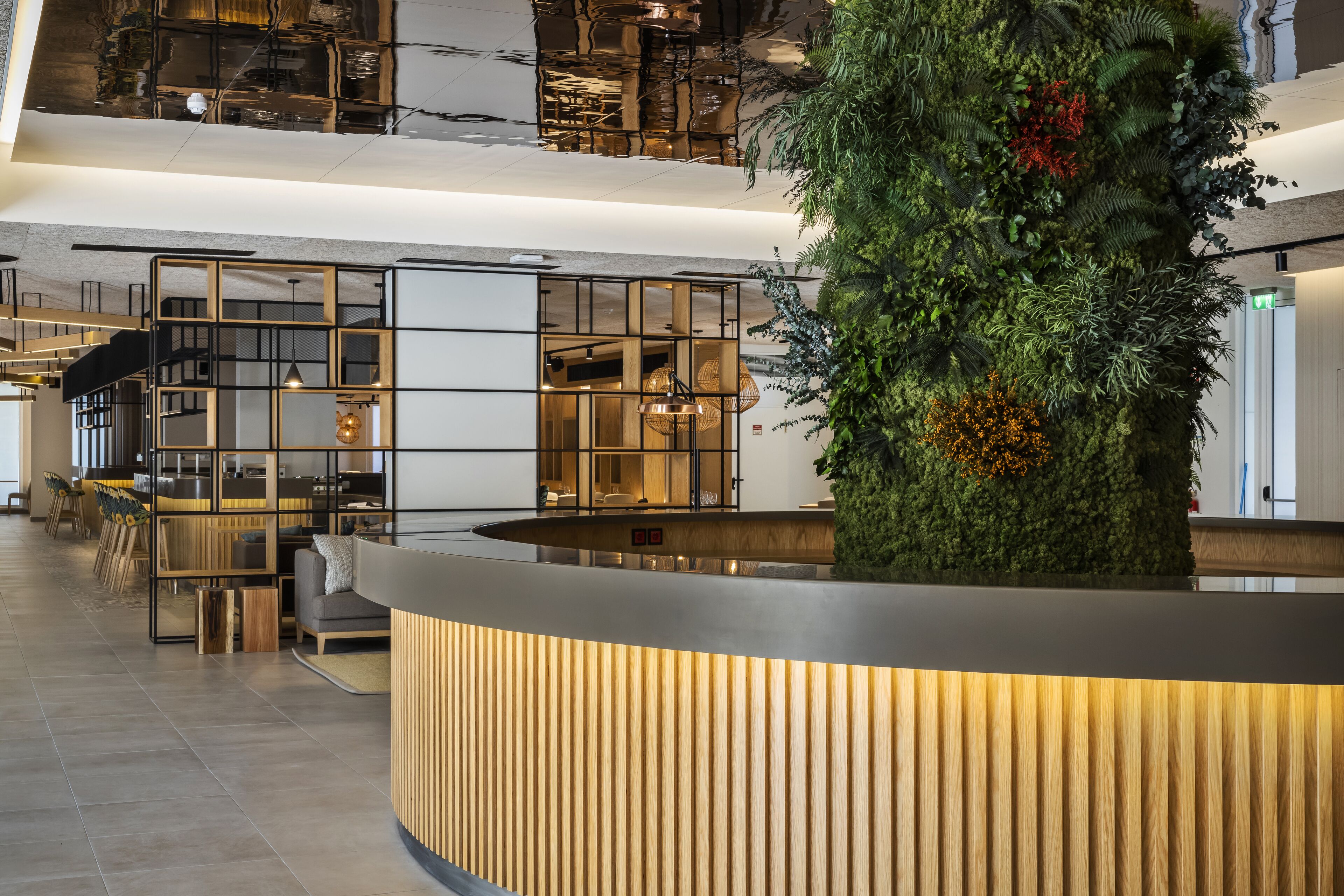A modern reception area with a curved reception desk, a vertical garden, and a seating area with chairs and tables.
