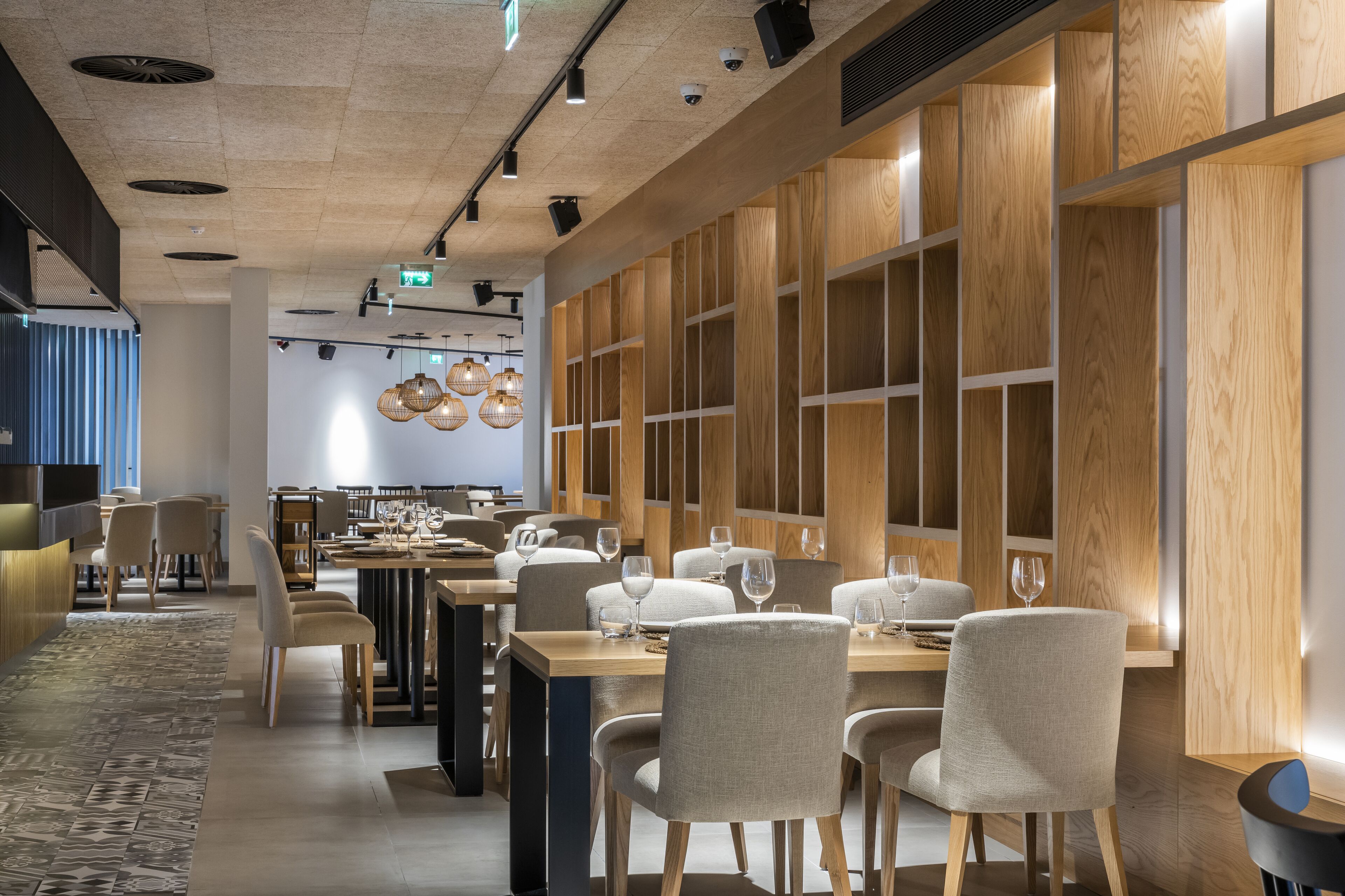 Een modern restaurant met houten lambrisering, meerdere eettafels met stoelen en hangende吊り灯.