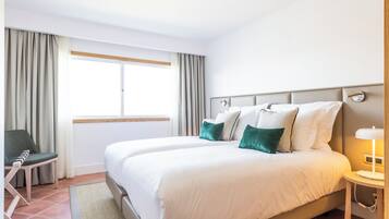 A hotel room with a large bed, a chair, a bedside table with a lamp, and a window with curtains.