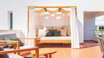 A sunlit outdoor seating area with a cushioned sofa, wooden chairs, and a small round table.
