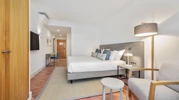 A modern hotel room with a bed, bedside table, lamp, chair, and a desk with a chair.