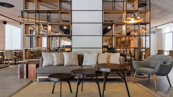 Un intérieur moderne avec un canapé, deux tables rondes et une chaise. On y trouve également des étagères et un luminaire suspendu.